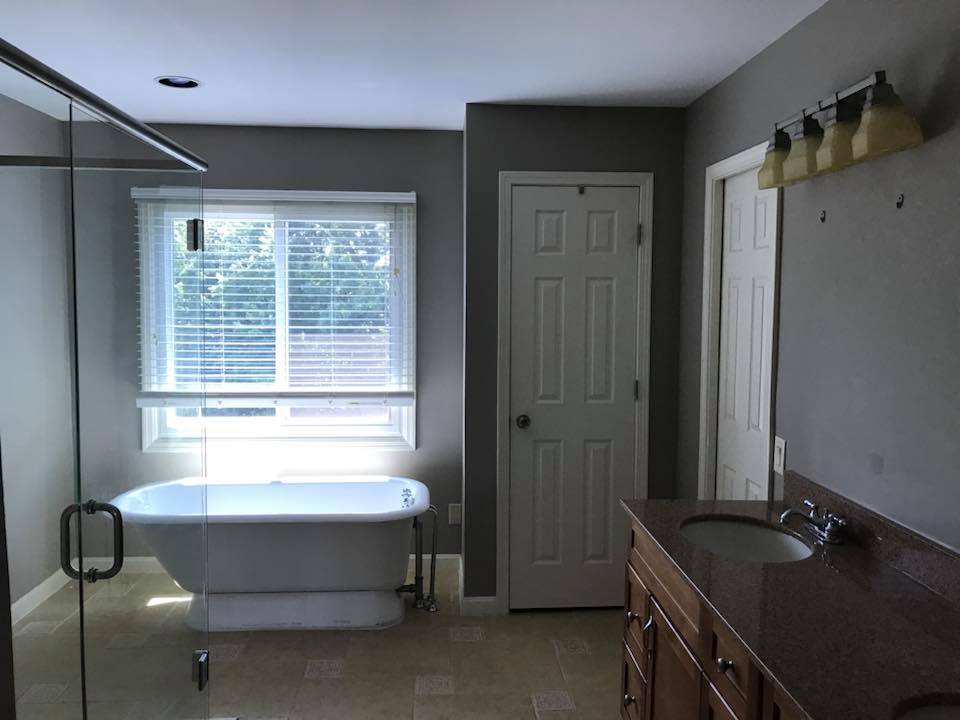 bathtub by window, glass shower in bathroom with grey walls and white doors