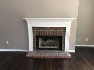 brick fire place with white mantel and white wall trim, grey walls, hardwood floor