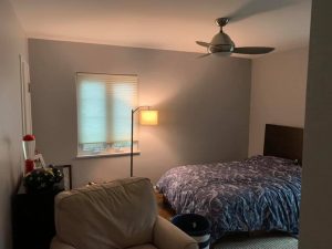 bedroom with ceiling fan blue comforter and large beige chair