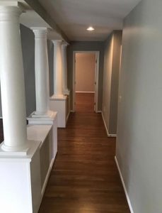 white narrow hallway with large columns on the left and wood floors
